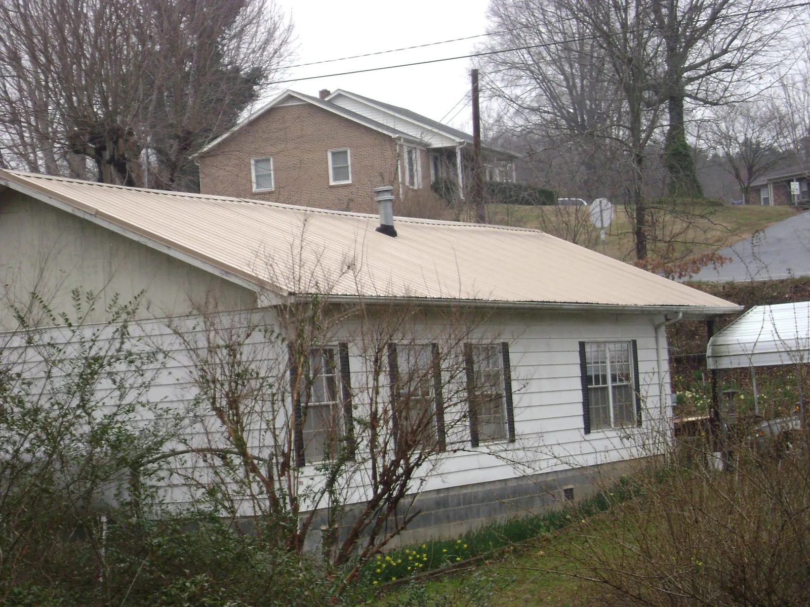 Tan metal roof on a white sided house set into a hillside — Commercial Roofing by Roofing Brothers in Atlantic Highlands